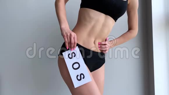 贴身的女性与适合苗条的身体在内裤持有白色卡片与文字SOS靠近她的胃视频的预览图