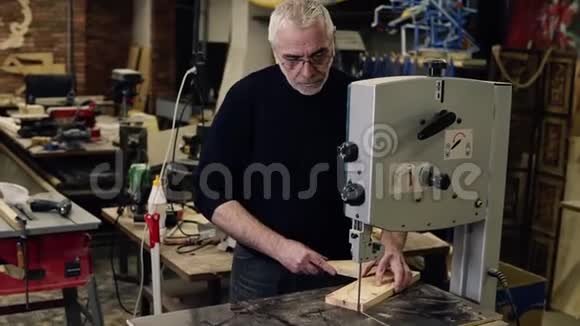 一位成年灰发男子在一间工作室里用铣床雕刻木图案时的肖像视频的预览图