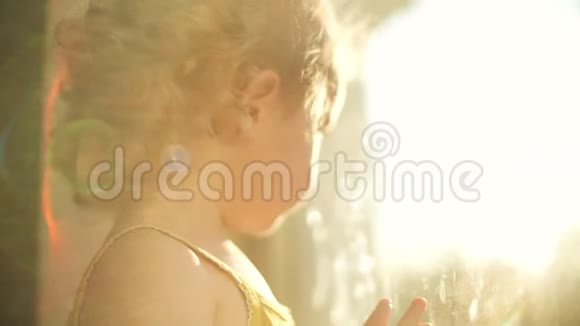 可爱的卷发金发女婴在家透过窗户为照相机微笑视频的预览图