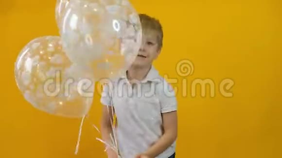快乐的小男孩蹒跚学步带着气球跳舞背景是黄色的视频的预览图