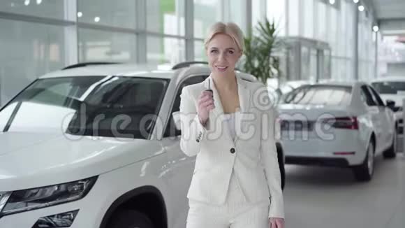 自信的年轻金发女人在镜头前拿出汽车钥匙微笑着穿白色西装的女商人买车视频的预览图
