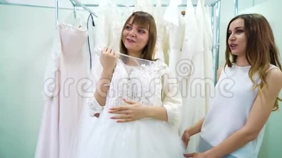年轻女孩和朋友在婚纱沙龙中选择婚纱视频的预览图