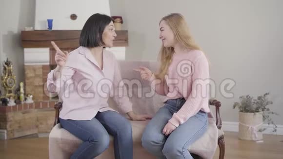 年轻的黑发白种人女人在室内和金发女孩有感情地交谈妈妈和女儿在家休息信托基金视频的预览图