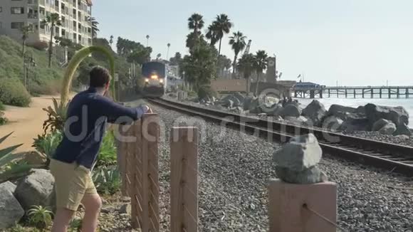 一个英俊的年轻人一个穿着海军蓝衬衫穿着短裤看着加州海岸圣克莱门特琳达莱恩公园的火车视频的预览图