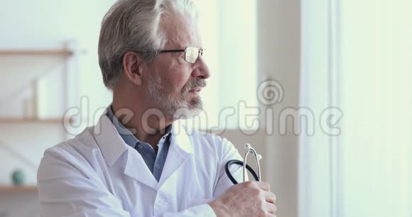 体贴的高级医生拿着听诊器透过窗户看视频的预览图