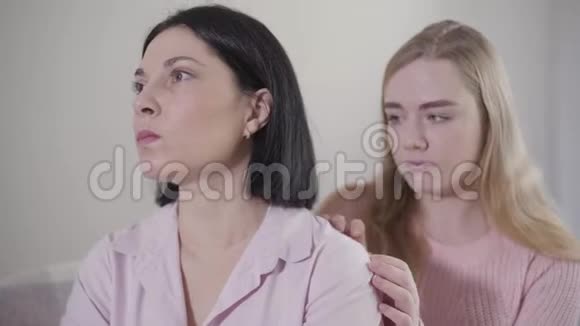 一幅悲伤的白种人女人的肖像当她十几岁的金发女儿抚摸她的肩膀时她望着别处多嘴多舌的女孩视频的预览图