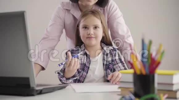 镜头接近漂亮的白人女学生坐在桌子旁拿着笔布鲁内特无法辨认的母亲视频的预览图