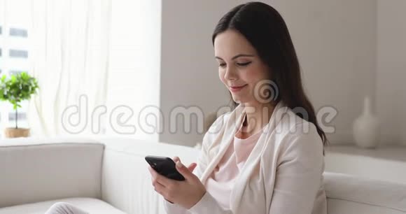 幸福的女人在家里查看社交媒体上的智能手机视频的预览图