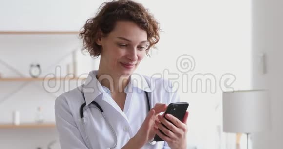 快乐的女治疗师穿着白色外套使用智能手机应用程序视频的预览图