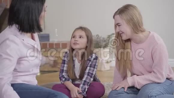 漂亮的白人女孩坐在柔软的地毯上和妈妈和姐姐玩的肖像孩子花时间视频的预览图