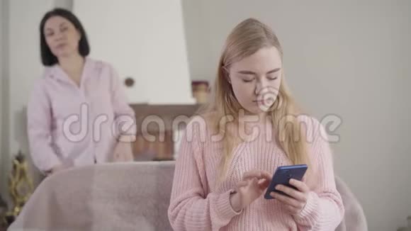 白种人迷人的金发女孩使用智能手机作为成年女性来到背景和看屏幕的肖像视频的预览图
