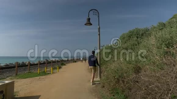 一个英俊的年轻人一个穿着海军蓝衬衫短裤和眼镜的男人在加利福尼亚海岸的圣岛上走着灯笼旋转视频的预览图