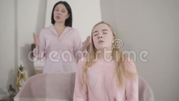 一幅美丽的金发白种人女孩坐在前台听着成年女人对她大喊大叫的画像视频的预览图