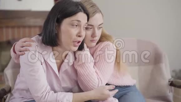 深色白种人女人坐在沙发上和金发女孩聊天的特写侧景少女镇静视频的预览图