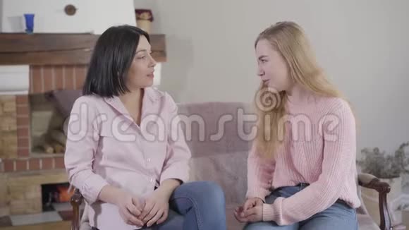 侧面看白种人母亲和十几岁的女儿坐在沙发上聊天微笑女孩和妈妈在一起视频的预览图