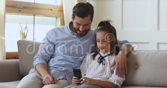 爸爸抱着小学校的小女孩看着有趣的视频视频的预览图