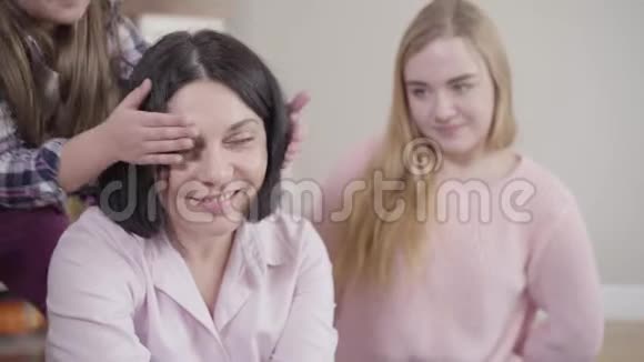 两个白人女儿给他们可爱的母亲送惊喜礼物快乐的黑发女人在家接受礼物视频的预览图