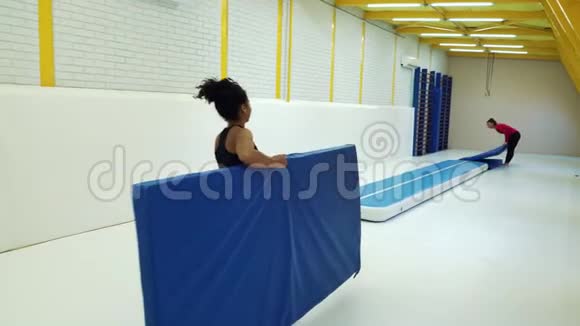 女子运动员在体育馆准备体操训练用垫视频的预览图
