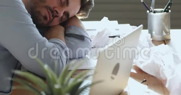 疲惫的商人睡在工作场所凌乱的书桌上视频的预览图