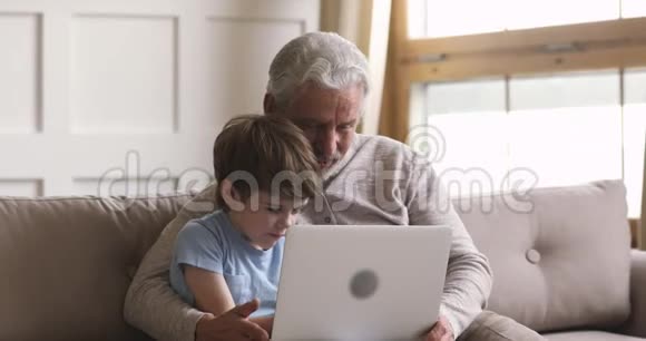 微笑的小儿子和爷爷在家看电影视频的预览图
