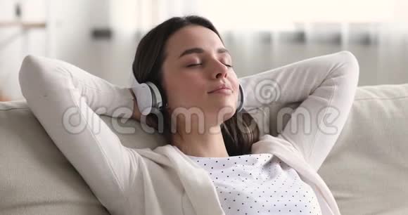 冷静放松的年轻女子戴着耳机在沙发上发冷视频的预览图
