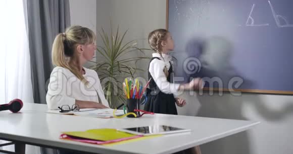 勤奋的白人女学生转向黑板用粉笔写作坐在餐桌前的成年女性视频的预览图