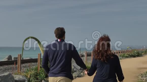 快乐的情侣在海滩上牵手享受美丽的一天前往太平洋冲浪铁路旅游假期视频的预览图