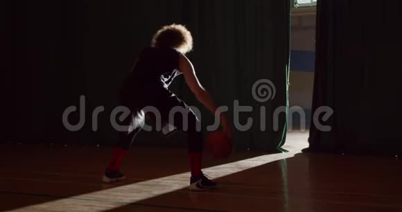 一个头发卷曲的白人篮球运动员准备进入地板剪影黑暗的后台光束视频的预览图