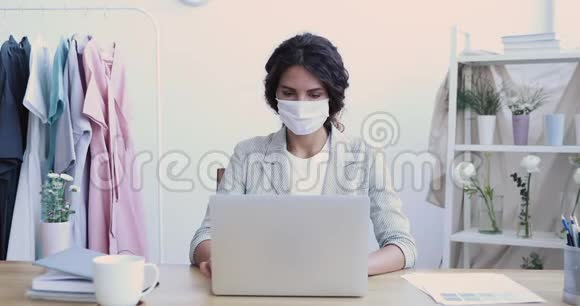 年轻女商人戴着面具的时装设计师在电脑上工作视频的预览图