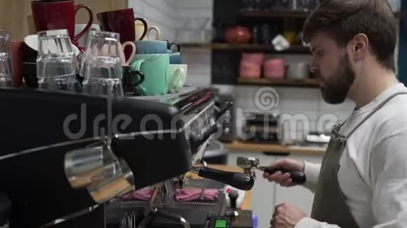 一个留着胡子的男咖啡师站在咖啡机旁边用严肃的表情煮咖啡视频的预览图
