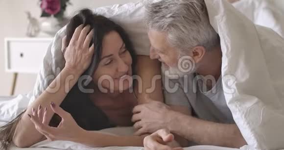 微笑的高加索族夫妇躺在白色毯子下揉鼻子的特写肖像幸福的丈夫视频的预览图