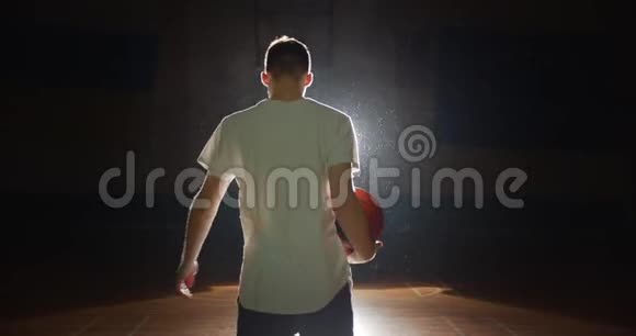 篮球运动员的剪影在手指上旋转一个球阴影黑暗后视视频的预览图