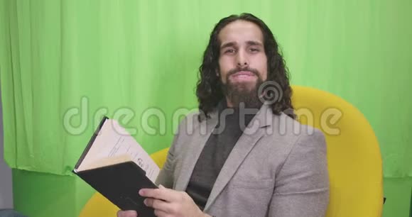 有思想的中东男子坐在黄色扶手椅上的书的肖像年轻男作家穿着正装视频的预览图