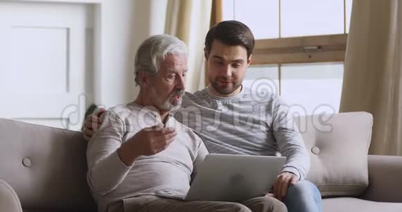 年轻人用电脑帮助成熟的父亲视频的预览图