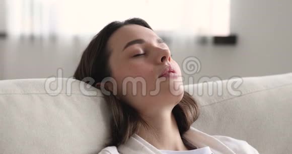 躺在舒适的沙发上睡着的轻松的年轻女子午睡视频的预览图