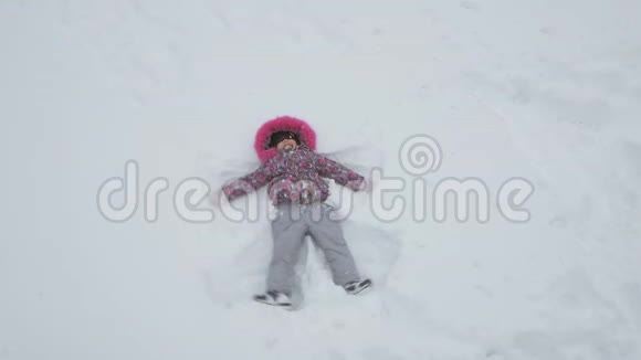 快乐的小女孩躺在雪地上做雪天使视频的预览图