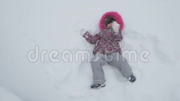 快乐的小女孩冬天在外面玩耍躺在雪地里爬行视频的预览图