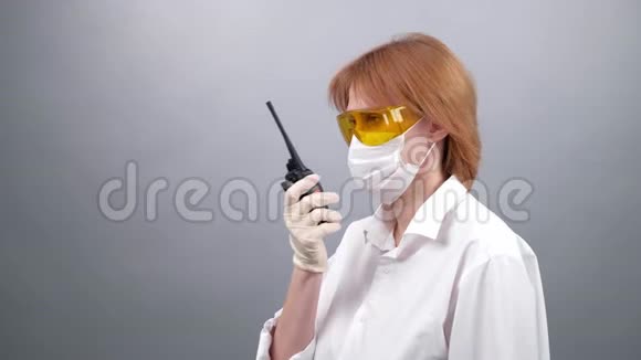 戴着安全眼镜医用口罩和橡胶手套的妇女在对讲机上讲话或在便携式收音机上讲话视频的预览图