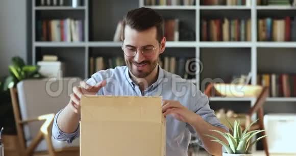 微笑的年轻人顾客打开包裹盒坐在桌子上视频的预览图