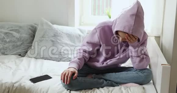 沮丧的少女独自坐在家里带着智能手机视频的预览图