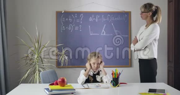 精疲力竭的白种人女孩扎着辫子坐在桌子旁双手抱着头当中年家庭教师解释她的话视频的预览图