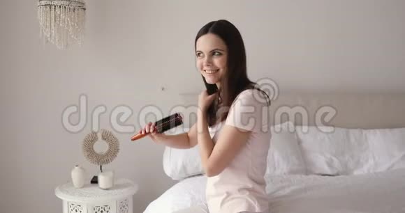 微笑迷人的少女梳着健康的头发坐在床上视频的预览图