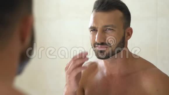 不快乐的男人在浴室镜子前检查脸上的皱纹衰老视频的预览图