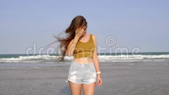 穿着牛仔裤的微笑的年轻女子在热带海洋海岸扎紧头发视频的预览图