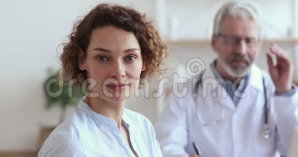 健康微笑的欧洲女人坐在医生面前看着摄像机视频的预览图