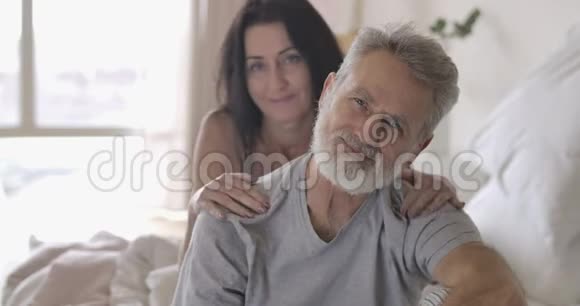 黑发高加索老太太拥抱着白发苍苍的英俊丈夫恋爱中的成熟夫妇在卧室里度过早晨视频的预览图