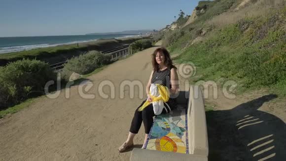 女人快乐美丽阳光明媚夏日坐在五颜六色的长凳上在海洋海岸旅行假期退休视频的预览图
