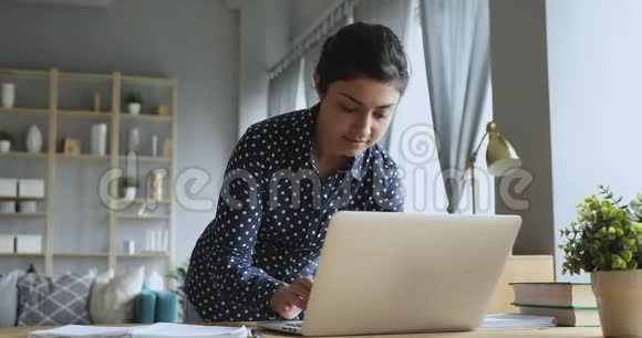 年轻的印度教女集中精力站在桌上的笔记本电脑上工作视频的预览图