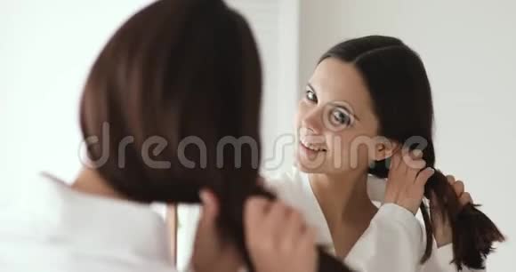 微笑年轻美丽的女人抚摸健康的头发照镜子视频的预览图