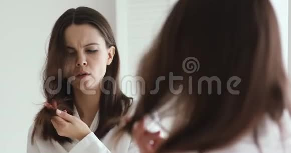沮丧的年轻女子梳着头发看着分叉的末端视频的预览图